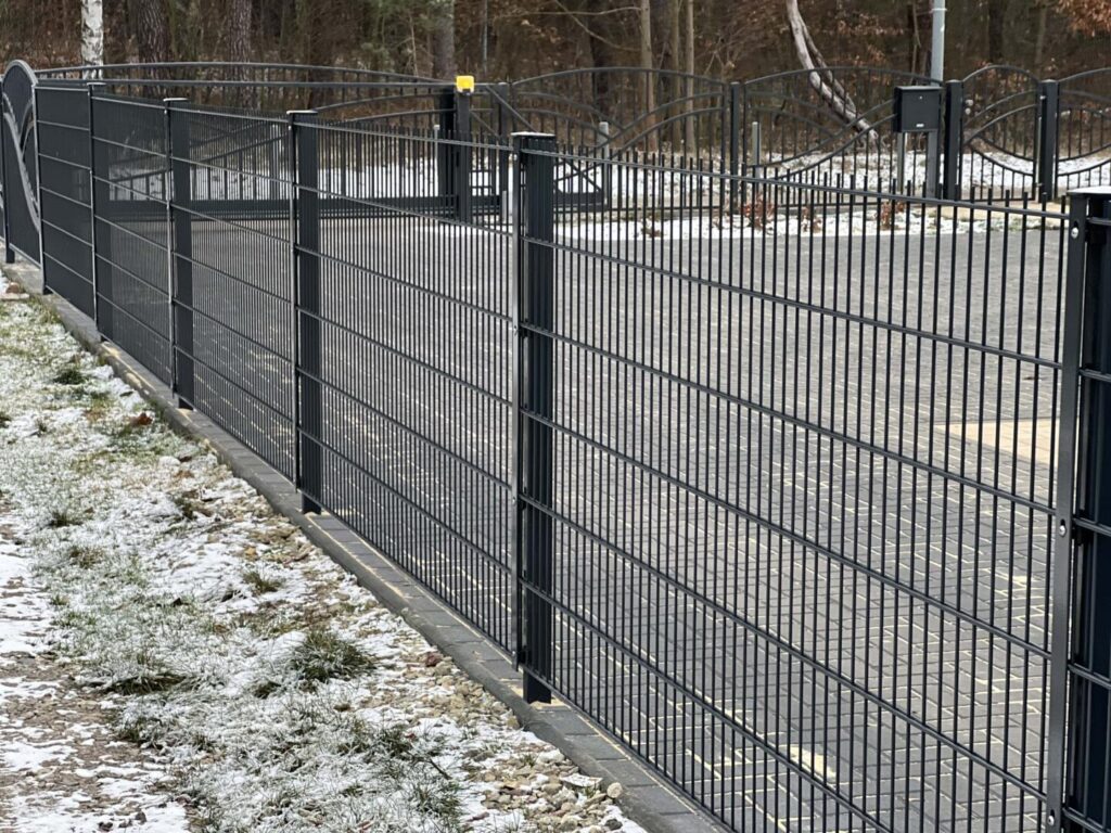 Schwarzer Metallzaun entlang gepflasterter Einfahrt im Winter