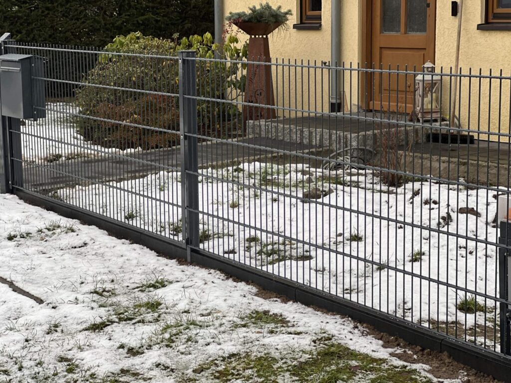 Metallzaun vor einem Haus im winterlichen Garten