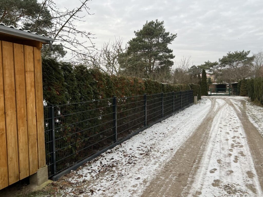 Verschneiter Weg neben Holzhütte und Metallzaun