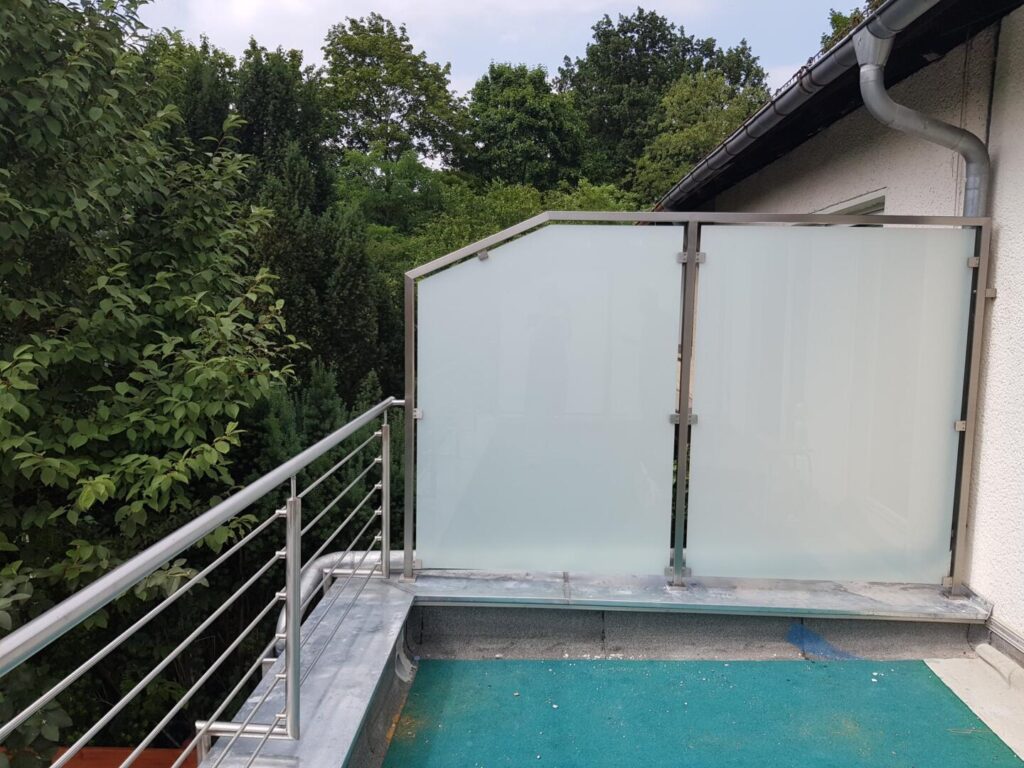 Balkon mit Glasgeländer und Blick auf grüne Bäume