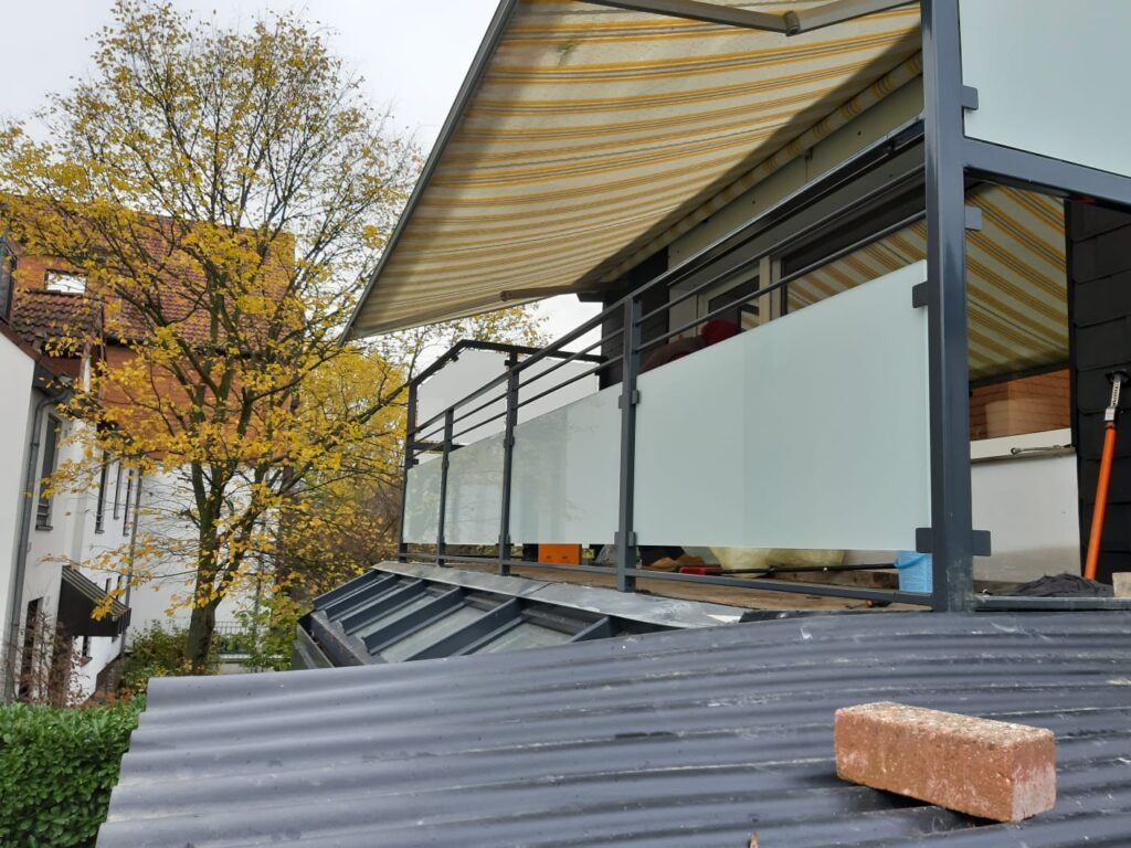 Moderner Balkon mit Glasgeländer und Markise.
