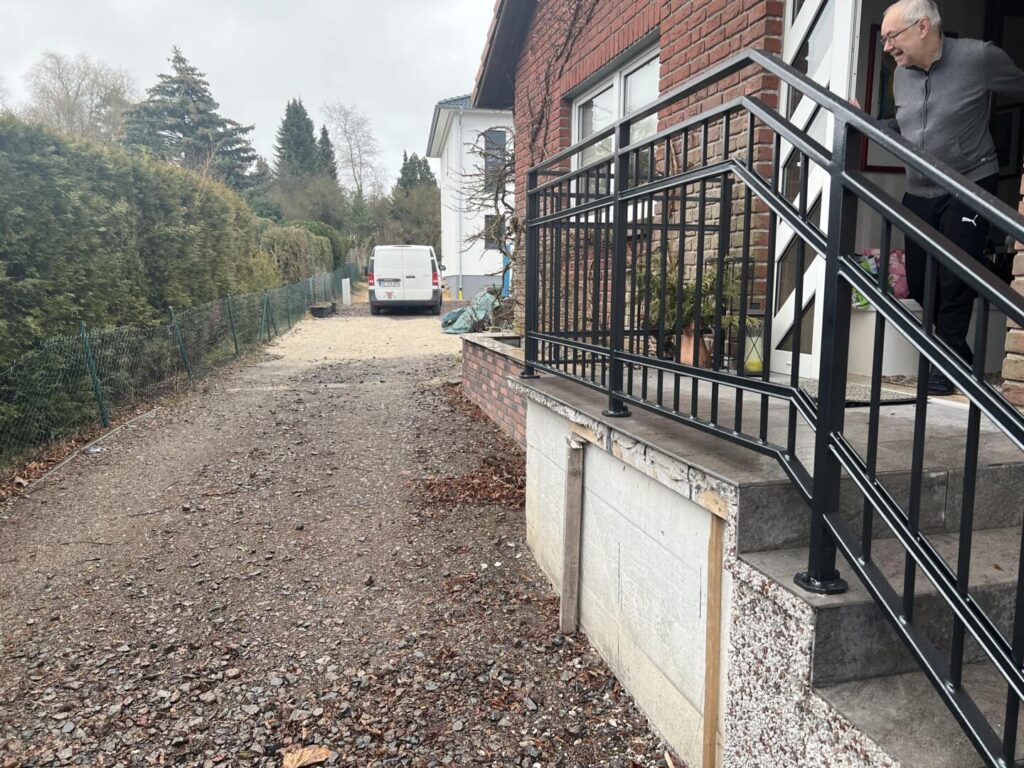 Mann steht vor Backsteinhaus mit Treppe und Einfahrt.