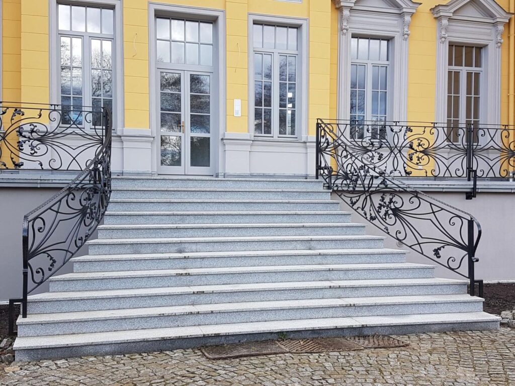 Steintreppe mit Schmiedeeisengeländer vor gelbem Gebäude