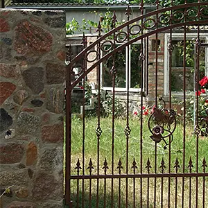 Eisernes Gartentor neben einer Steinmauer mit Rosen