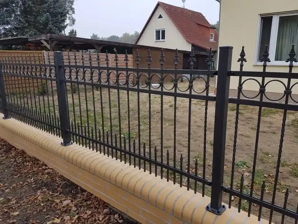 Schwarzer Metallzaun vor Wohnhaus und Garten
