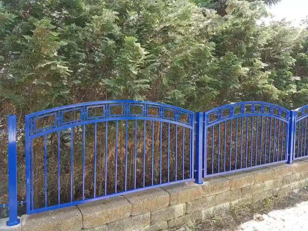 Blauer Metallzaun vor grünen Büschen