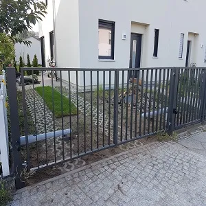 Metallzaun vor modernem Wohnhaus mit Gartenweg
