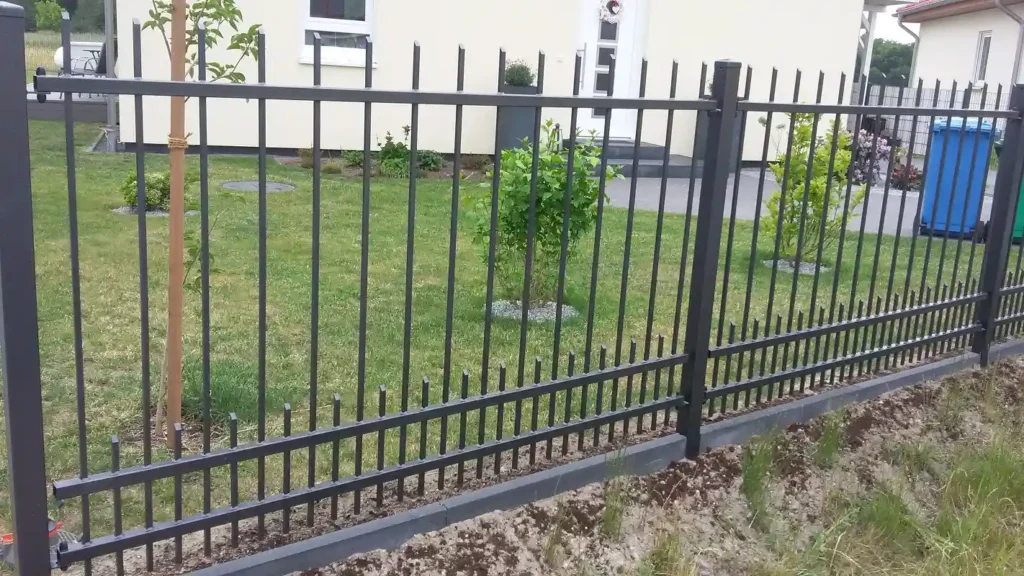 Metallzaun vor Haus mit grünem Garten