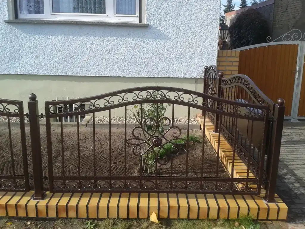 Metallzaun mit Ziegelmauer vor einem Haus