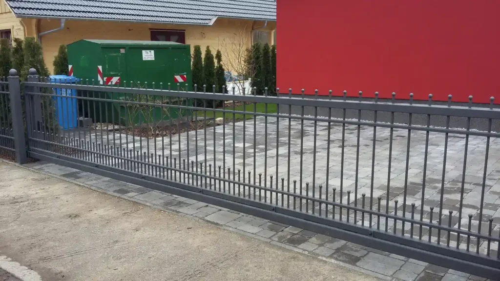 Graues Metalltor vor modernem Haus und Hofpflaster