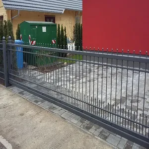 Metallzaun vor modernem Haus mit gepflasterter Einfahrt